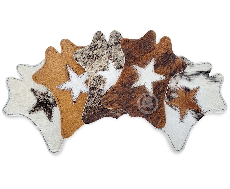 May include: Six cowhide coasters in a range of colours, including white, brown, and tan. Each coaster has a stitched white star and a stitched border. The coasters are arranged in a fan shape.