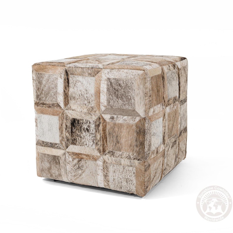 K&ouml;nnte beinhalten: Ein quadratischer Hocker mit einem Patchwork-Design aus verschiedenen Braunt&ouml;nen und Wei&szlig;t&ouml;nen aus Kuhfell. Der Hocker ist aus Leder und hat ein geometrisches Muster.