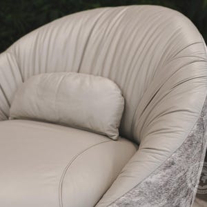May include: A light gray leather armchair with a matching pillow. The chair has a rounded back and a tufted design. The chair is accented with a gray and white cowhide trim.