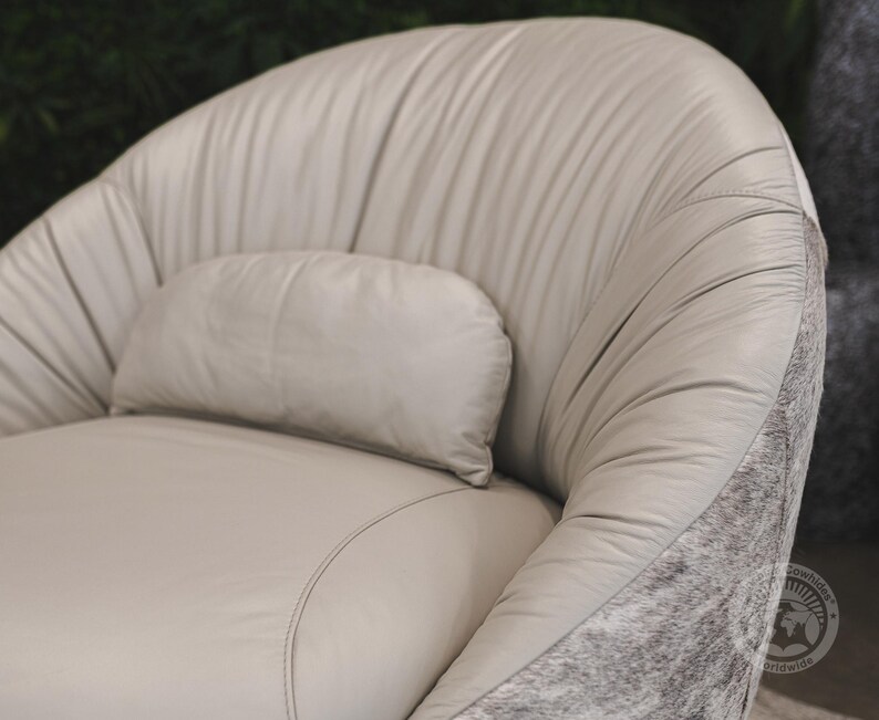 May include: A light gray leather armchair with a matching pillow. The chair has a rounded back and a tufted design. The chair is accented with a gray and white cowhide trim.