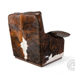 May include: A brown leather armchair with a cowhide pattern on the back and seat. The chair has a wooden base and a pillow on the armrest.