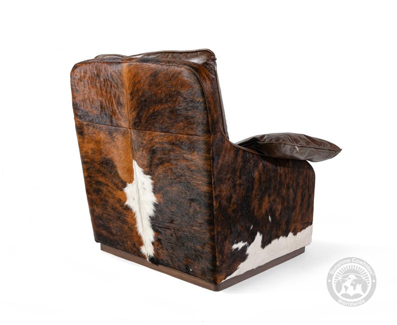 May include: A brown leather armchair with a cowhide pattern on the back and seat. The chair has a wooden base and a pillow on the armrest.