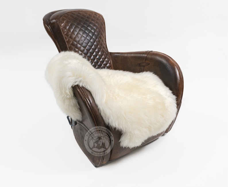 Puede incluir: Un sill&oacute;n de cuero marr&oacute;n con respaldo acolchado en forma de diamante y una manta de piel de oveja color crema sobre el asiento. La silla tiene una est&eacute;tica vintage y est&aacute; sobre un fondo blanco.