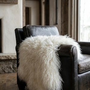 Puede incluir: Un sill&oacute;n de cuero marr&oacute;n oscuro con una manta de piel sint&eacute;tica blanca y esponjosa sobre &eacute;l. La manta tiene fibras largas y peludas. La silla est&aacute; en una habitaci&oacute;n con chimenea y detalles de madera.