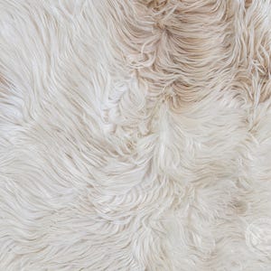 May include: A long-pile faux fur rug featuring a blend of cream, off-white, and light beige tones. The texture consists of dense, wavy synthetic fibers that create a soft, layered appearance across the entire surface of the textile material.