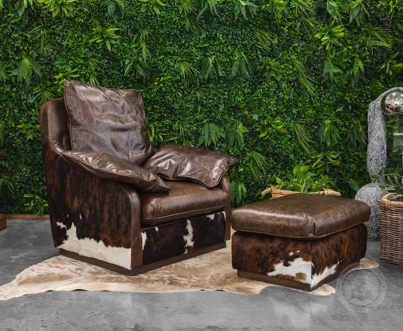 May include: A brown leather armchair with a cowhide pattern and a matching ottoman. The chair has a high back and a comfortable seat. The ottoman is a square shape and has a similar cowhide pattern.