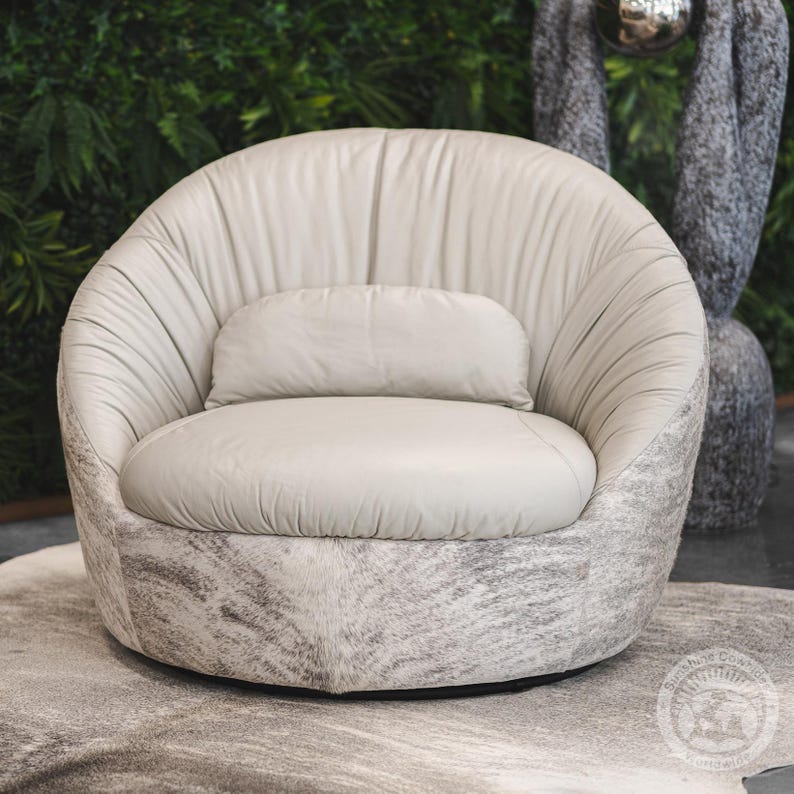 May include: A white leather swivel chair with a gray and white cowhide pattern on the base. The chair has a rounded back and a comfortable seat cushion.