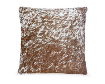 May include: Brown and white cowhide pillow with a brown leather tag that says "Genuine Cowhide".