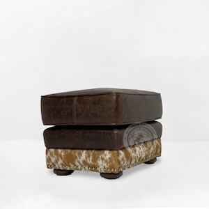 May include: A brown leather ottoman with a cowhide pattern on the bottom. The ottoman has a square shape and is decorated with gold studs.