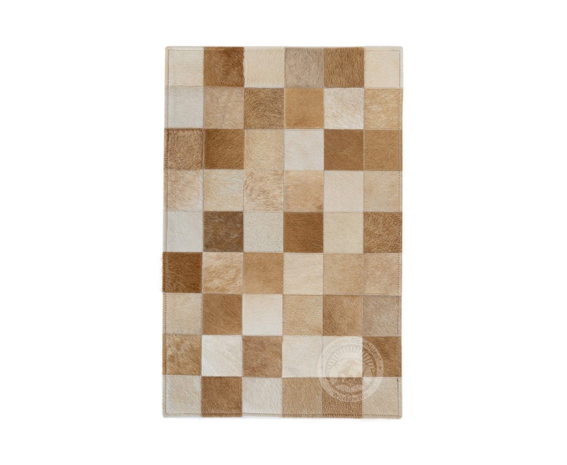 May include: A tan and white patchwork rug made of cowhide. The rug is made up of squares of different sizes and colors.