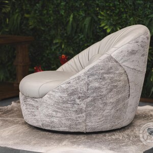 May include: A gray swivel chair with a white and gray cowhide upholstery. The chair is sitting on a white rug in front of a green wall.