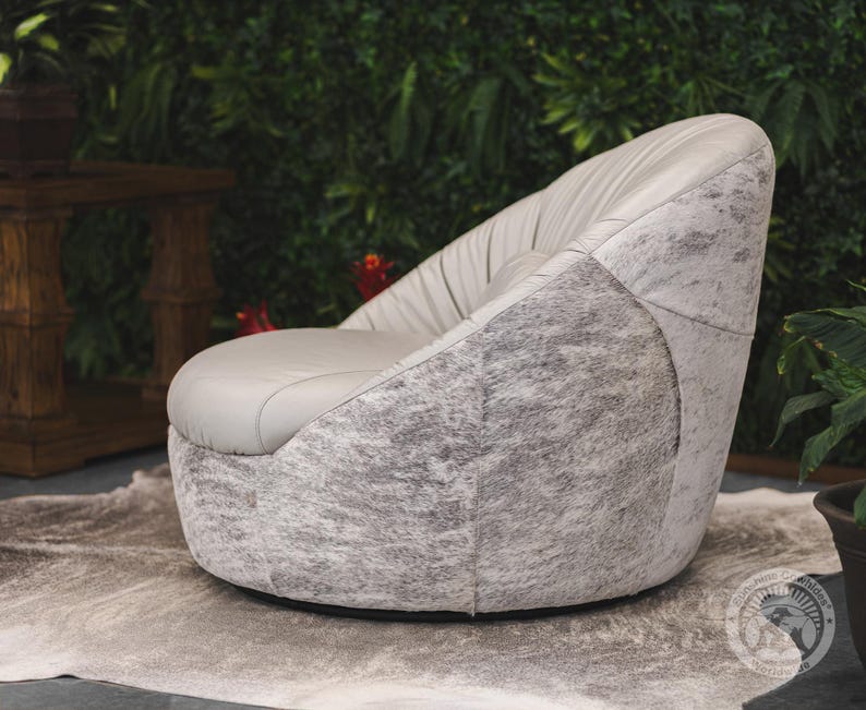 May include: A gray swivel chair with a white and gray cowhide upholstery. The chair is sitting on a white rug in front of a green wall.