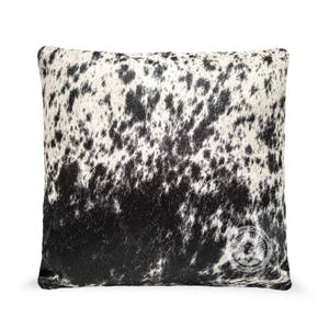 May include: Black and white cowhide pillow with a subtle pattern. The pillow is rectangular and has a soft, plush texture.