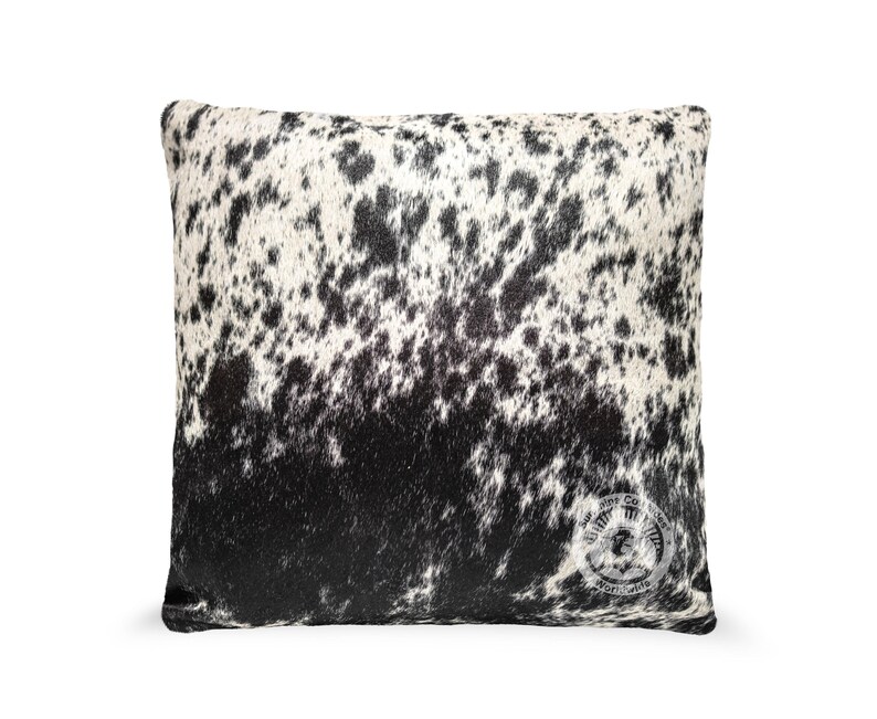 May include: Black and white cowhide pillow with a subtle pattern. The pillow is rectangular and has a soft, plush texture.
