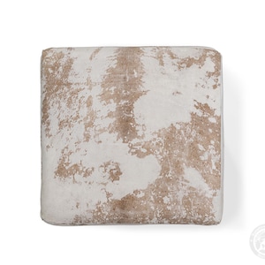 Puede incluir: Un coj&iacute;n de suelo cuadrado con un patr&oacute;n de piel de vaca natural con parches irregulares de pelo blanco y marr&oacute;n claro. El coj&iacute;n tiene una superficie superior plana y bordes definidos, mostrando una textura org&aacute;nica moteada en el panel.