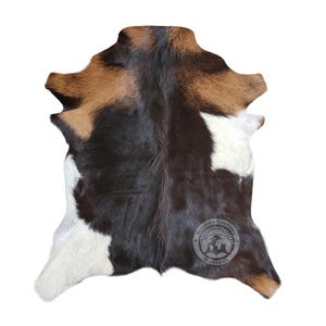 Puede incluir: Una alfombra de piel de vaca con parches negros, blancos y marrones. La alfombra mide aproximadamente 90 cm por 120 cm.