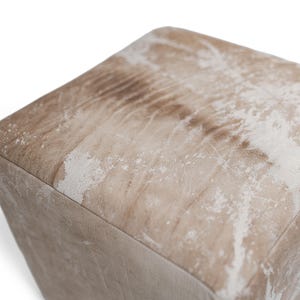 Puede incluir: Un puf cuadrado con un acabado desgastado en tonos marr&oacute;n claro y blanco. La superficie muestra una textura moteada y envejecida con patrones de grano visibles en la parte superior y los lados, creando una apariencia tonal en este mueble c&uacute;bico.