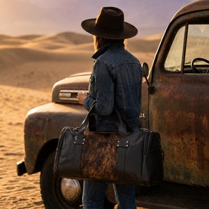 May include: A black leather duffel bag featuring a central panel of brown and black cowhide fur. The bag has two sturdy top handles, silver-toned metal hardware, and a rectangular shape with reinforced stitching along the sides and base.