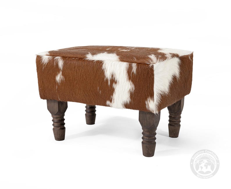 K&ouml;nnte beinhalten: Ein brauner und wei&szlig;er Kuhfell-Hocker mit vier gedrehten Holzbeinen.
