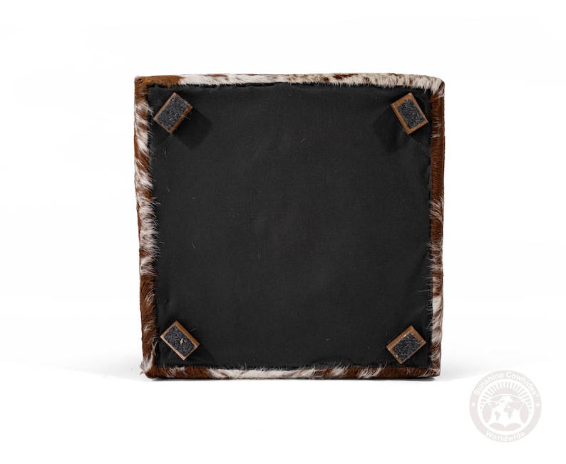 Pu&ograve; includere: Un pouf in pelle di mucca marrone e bianco con quattro piedini in legno marrone scuro.
