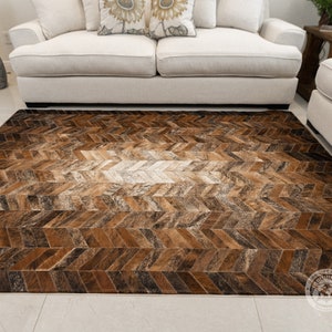 May include: A brown and white cowhide rug with a herringbone pattern. The rug is made from natural leather and has a rustic look.