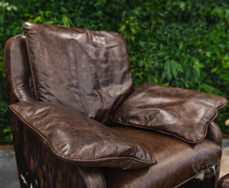 May include: A brown leather armchair with a tufted back and two large pillows. The chair is in front of a green wall.
