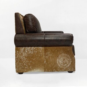 May include: A brown leather armchair with a cowhide base. The chair has a tufted back and a pillow. The chair is made by the "Western Cowboy" brand.