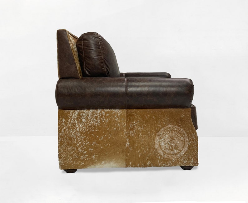 May include: A brown leather armchair with a cowhide base. The chair has a tufted back and a pillow. The chair is made by the "Western Cowboy" brand.