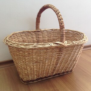 May include: A woven wicker basket with a single handle. The basket is oval shaped and has a light brown color.