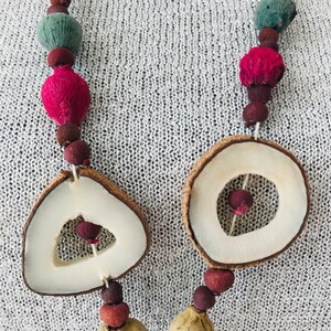 May include: A necklace made of natural materials, including dried fruit, seeds, and wood. The necklace features two large, round wooden beads with cut-out designs.