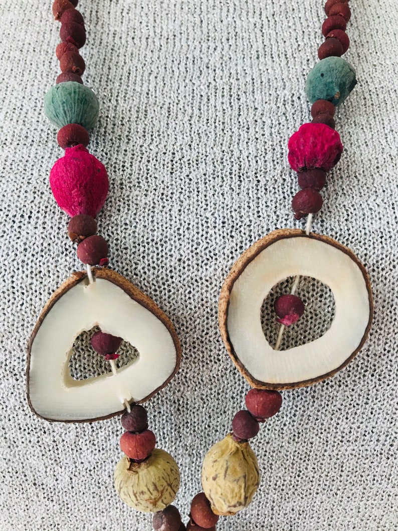 May include: A necklace made of natural materials, including dried fruit, seeds, and wood. The necklace features two large, round wooden beads with cut-out designs.