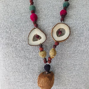 May include: A brown, natural wood necklace with round and triangular beads, and a large, round pendant. The necklace is made of various natural materials, including wood, seeds, and dried fruit.