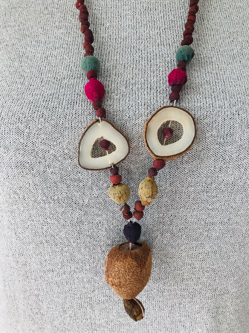 May include: A brown, natural wood necklace with round and triangular beads, and a large, round pendant. The necklace is made of various natural materials, including wood, seeds, and dried fruit.