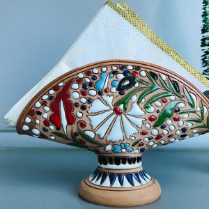 Pode incluir: Porta-guardanapos de cer&acirc;mica com um design floral em tons de vermelho, verde, azul e branco. O porta-guardanapos tem a forma de um leque e tem uma base.