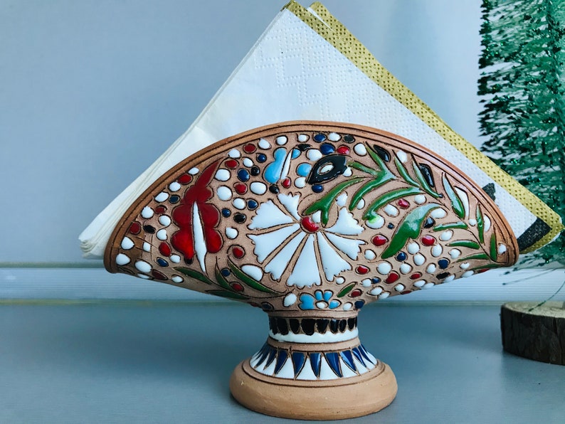 Pode incluir: Porta-guardanapos de cer&acirc;mica com um design floral em tons de vermelho, verde, azul e branco. O porta-guardanapos tem a forma de um leque e tem uma base.