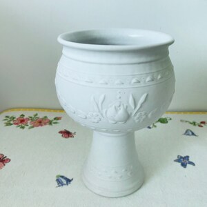May include: White ceramic planter with a pedestal base and embossed floral design.