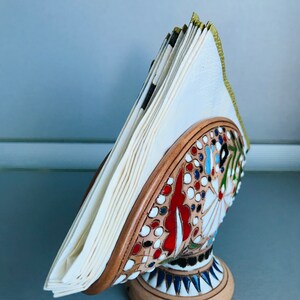 Pode incluir: Um porta-guardanapos de cer&acirc;mica com um design floral colorido. O porta-guardanapos tem a forma de um p&aacute;ssaro com um guardanapo branco dentro.