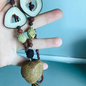 May include: A brown and beige necklace made of dried fruit and seeds. The necklace has a large brown seed at the bottom and two circular pieces of dried fruit at the top.