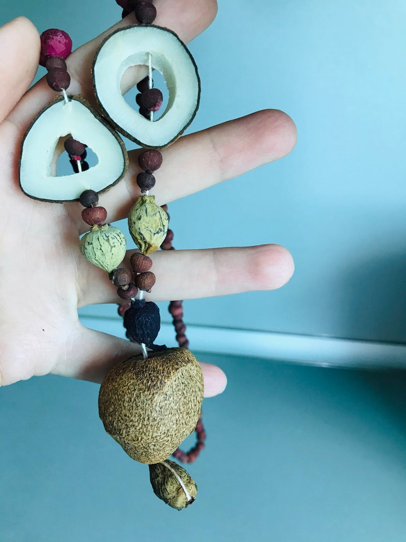 May include: A brown and beige necklace made of dried fruit and seeds. The necklace has a large brown seed at the bottom and two circular pieces of dried fruit at the top.