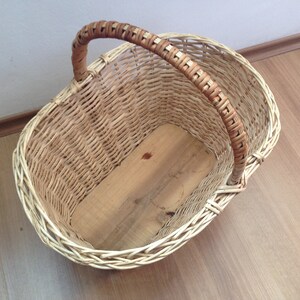 May include: A woven wicker basket with a brown handle. The basket is empty and has a wooden base.