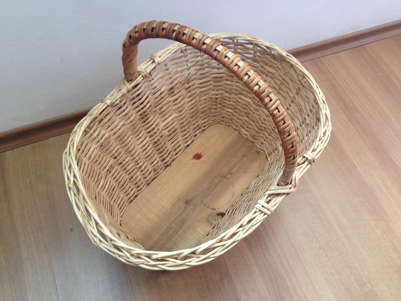 May include: A woven wicker basket with a brown handle. The basket is empty and has a wooden base.