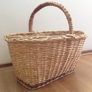 May include: A woven wicker basket with a natural brown color and a sturdy handle. The basket is oval shaped and has a wide opening.
