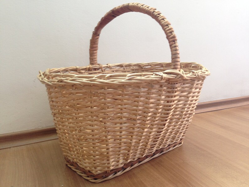 May include: A woven wicker basket with a natural brown color and a sturdy handle. The basket is oval shaped and has a wide opening.