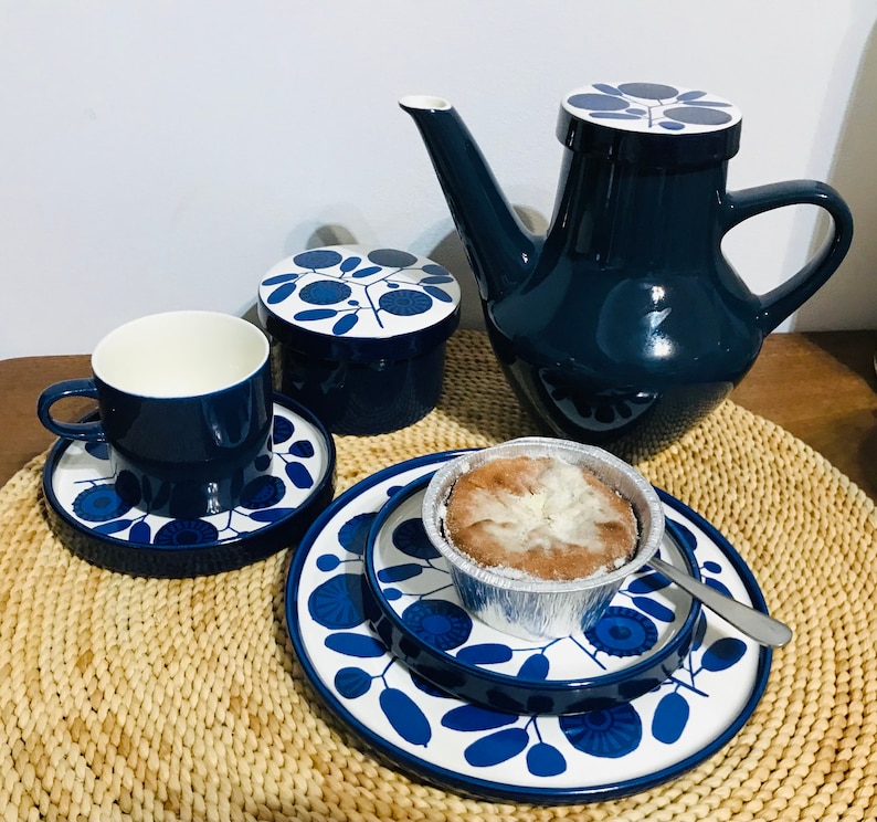 K&ouml;nnte beinhalten: Ein blaues und wei&szlig;es Teeservice mit floralem Muster, bestehend aus Teekanne, Zuckerdose, Tasse und Untertasse sowie einem kleinen Teller mit einem Geb&auml;ck.