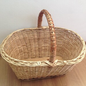 May include: A woven wicker basket with a natural brown handle. The basket is oval shaped and has a light brown color.