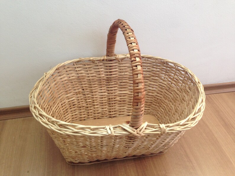 May include: A woven wicker basket with a natural brown handle. The basket is oval shaped and has a light brown color.