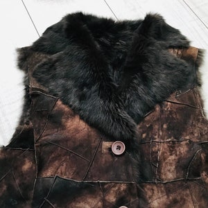 May include: A brown leather vest with a black fur collar. The vest is made of patchwork leather and has a button closure.