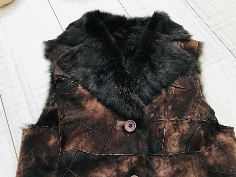 May include: A brown leather vest with a black fur collar. The vest is made of patchwork leather and has a button closure.