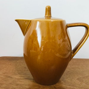 Könnte beinhalten: Eine braune Teekanne aus Keramik mit rundem Korpus und Deckel. Die Teekanne hat einen Henkel an der Seite und einen Ausguss vorne.