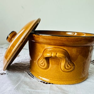 Puede incluir: Una olla de cerámica marrón con tapa y un asa decorativa. La olla tiene un acabado esmaltado y es perfecta para guardar alimentos.